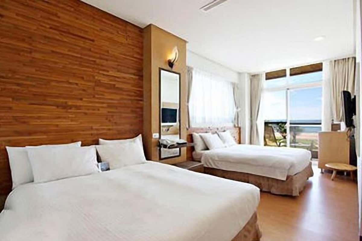 Habitación de hotel con dos camas, un panel decorativo de madera, un ventanal con vistas y una pequeña zona de estar.