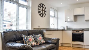 A modern kitchen with a built-in oven, a dining area with a leather sofa and patterned cushions, and a large wall clock. - 2 bedroom accommodation in Whitby (Whitby)