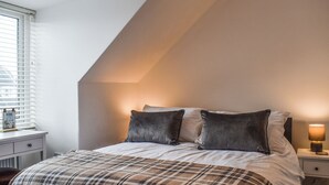 A bedroom with a bed, a nightstand, a lamp, and a window with blinds. - 2 bedroom accommodation in Whitby (Whitby)