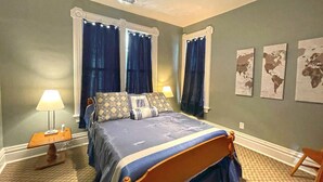 A bedroom with a large bed, two bedside lamps, a world map on the wall, and a carpeted floor.