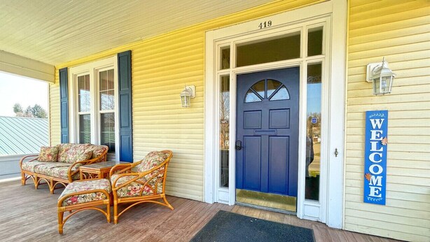 A yellow building with a blue door, numbered 419, and a 'WELCOME' sign. There are wicker chairs and a doormat in front.
