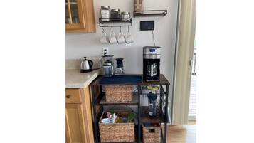 A kitchen with a coffee maker, kettle, and storage baskets on a metal cart.