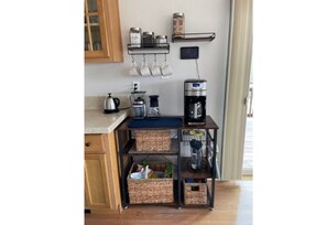 Una cocina con cafetera, hervidor y cestas de almacenamiento sobre un carrito metálico.
