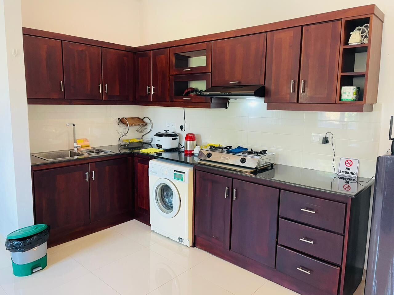 A kitchen with dark wooden cabinets, a washing machine, a microwave, and a stove.