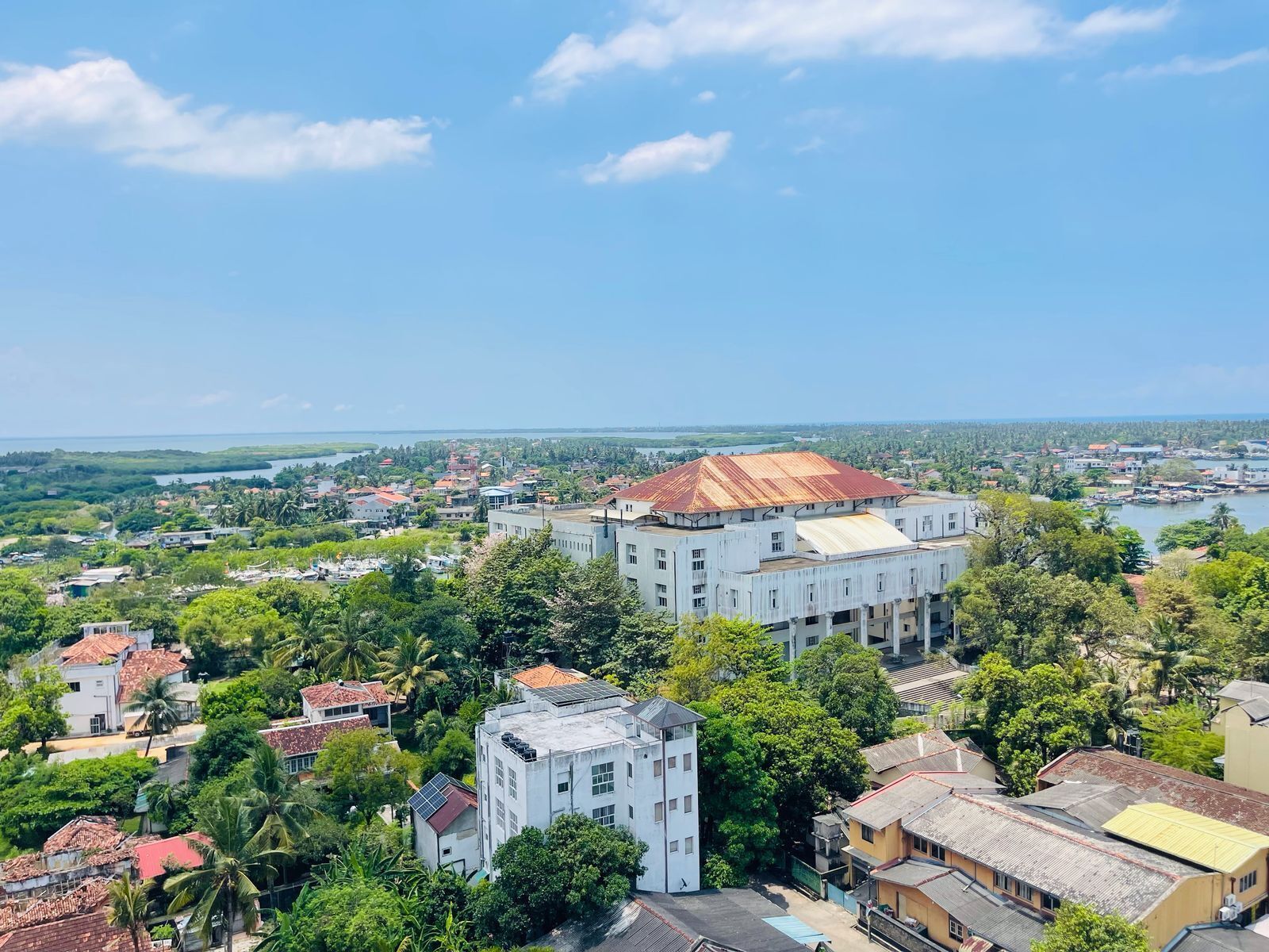 A coastal town with a prominent white building with a red roof, surrounded by lush greenery and residential houses.