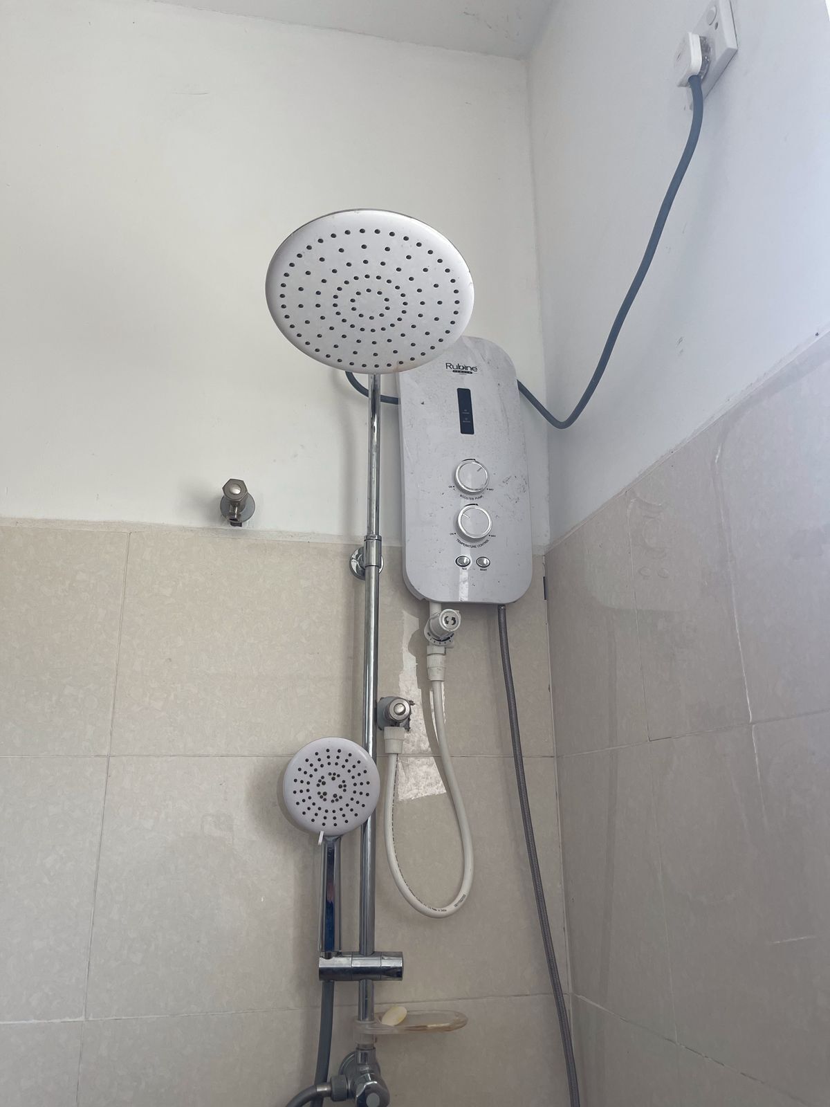 Un baño con ducha, que incluye un cabezal de ducha manual y un cabezal de ducha fijo en la pared, conectado a un panel de control con varios botones.