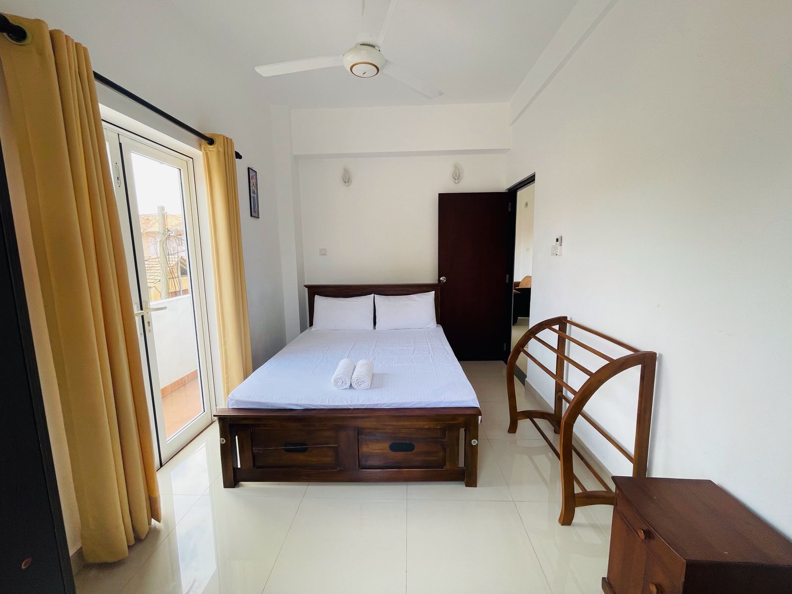 A hotel room with a bed, a wooden nightstand, a ceiling fan, and a sliding glass door with curtains.