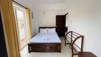 A hotel room with a bed, a wooden nightstand, a ceiling fan, and a sliding glass door with curtains.