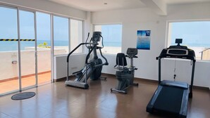 Une salle de sport équipée de machines de cardio, dotée de grandes fenêtres et offrant une vue sur la mer.