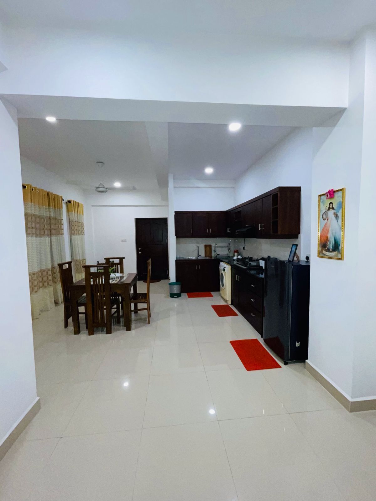A spacious living area with a dining table and chairs, a kitchen with dark cabinets, and a red rug.
