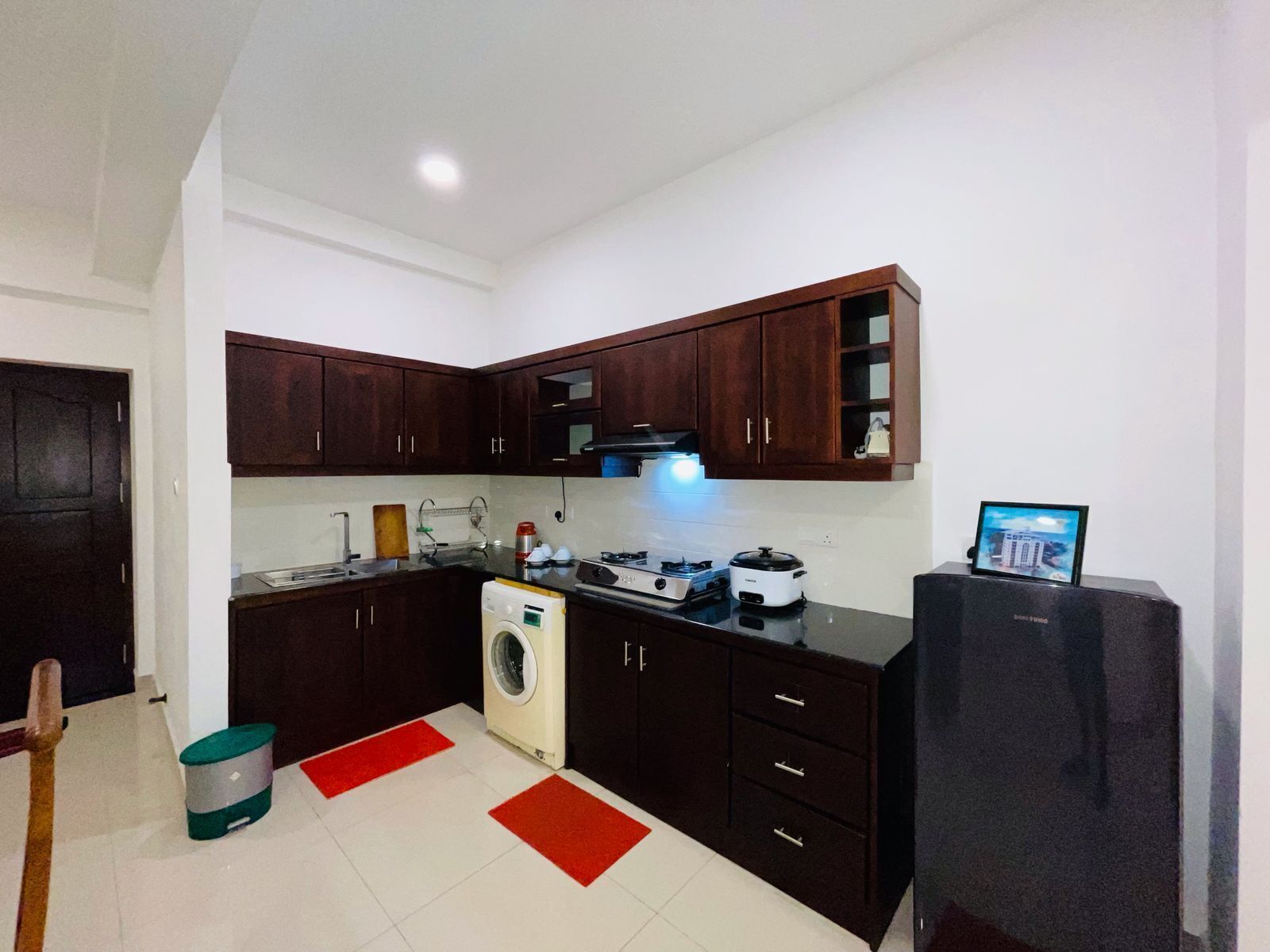A compact kitchen with dark wooden cabinets, a washing machine, a stove, and a refrigerator.