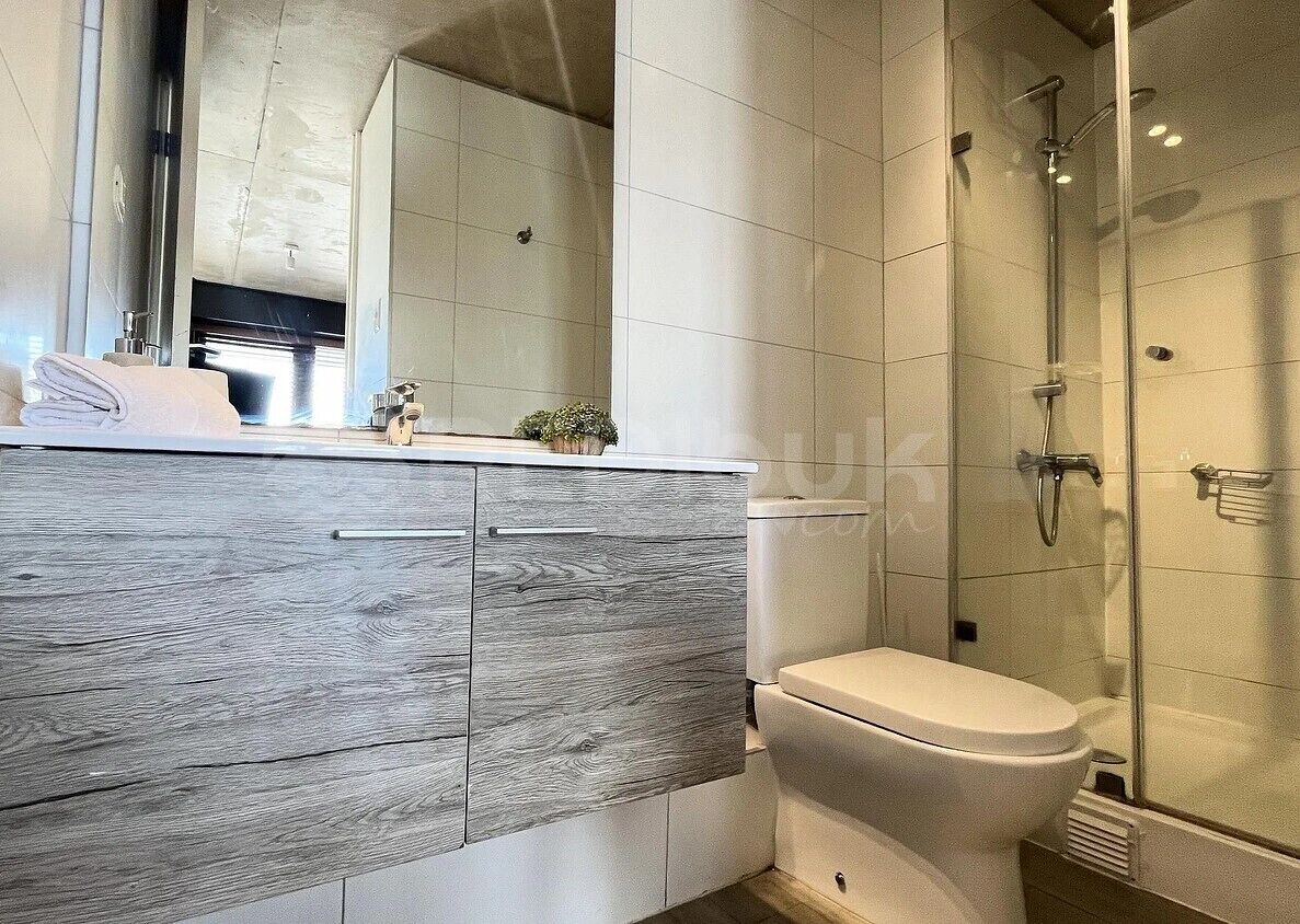 Un baño moderno con un tocador de madera, un inodoro y una zona de ducha con mampara de vidrio.