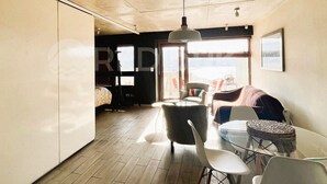 A modern living room with a dining area, large windows, and a ceiling with exposed beams.