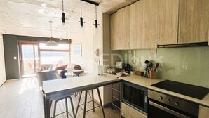 A modern kitchen with a large island, a built-in oven, and a microwave. There is a window providing natural light and a view of the outdoors.