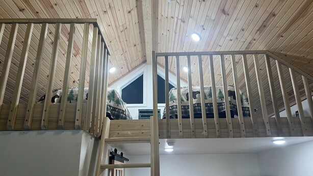 A loft bedroom with a wooden ceiling, a bunk bed, and a ladder.
