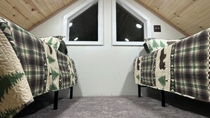 A cozy attic room with a sloped ceiling, two windows, and a carpeted floor.