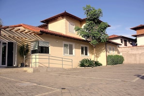 Uma casa de dois andares com telhado de telhas, varanda e entrada pavimentada.
