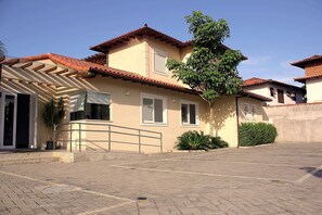 A two-story house with a tiled roof, a balcony, and a paved driveway. - Bz02 Casa Moderna 250m da praia Geribá (Búzios)