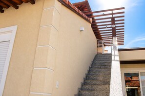 A staircase leading to a covered outdoor area with a wooden pergola and a clear blue sky.