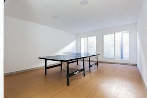Quarto com mesa de pingue-pongue, grandes janelas e piso de madeira.