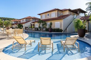 A pool area with lounge chairs and a building with a tiled roof. - Bz02 Casa Moderna 250m da praia Geribá (Búzios)