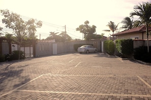 Uma entrada com portão ao final de um caminho de paralelepípedos, com um carro estacionado.
