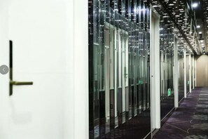 Um corredor com divisórias de vidro, piso carpete e uma porta à esquerda.