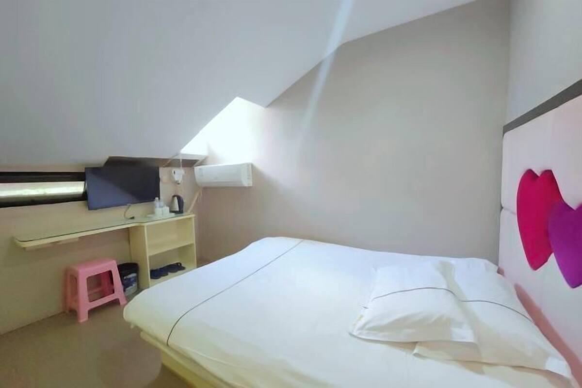 Een kleine, netjes ingerichte kamer met een bed, een bureau en een roze kruk.