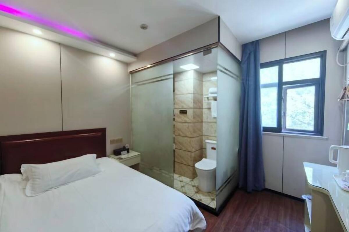 Een hotelkamer met een bed, een douchecabine, een toilet, een raam en een nachtkastje.
