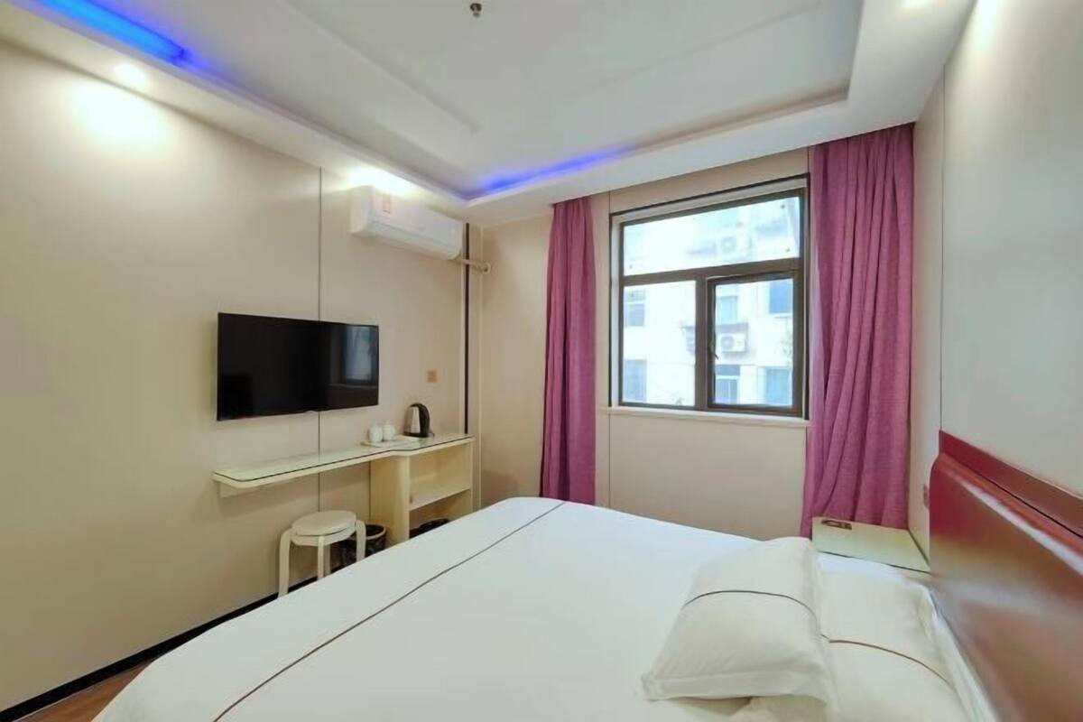 Een hotelkamer met een bed, een televisie, een bureau, een raam met gordijnen en een airconditioner.