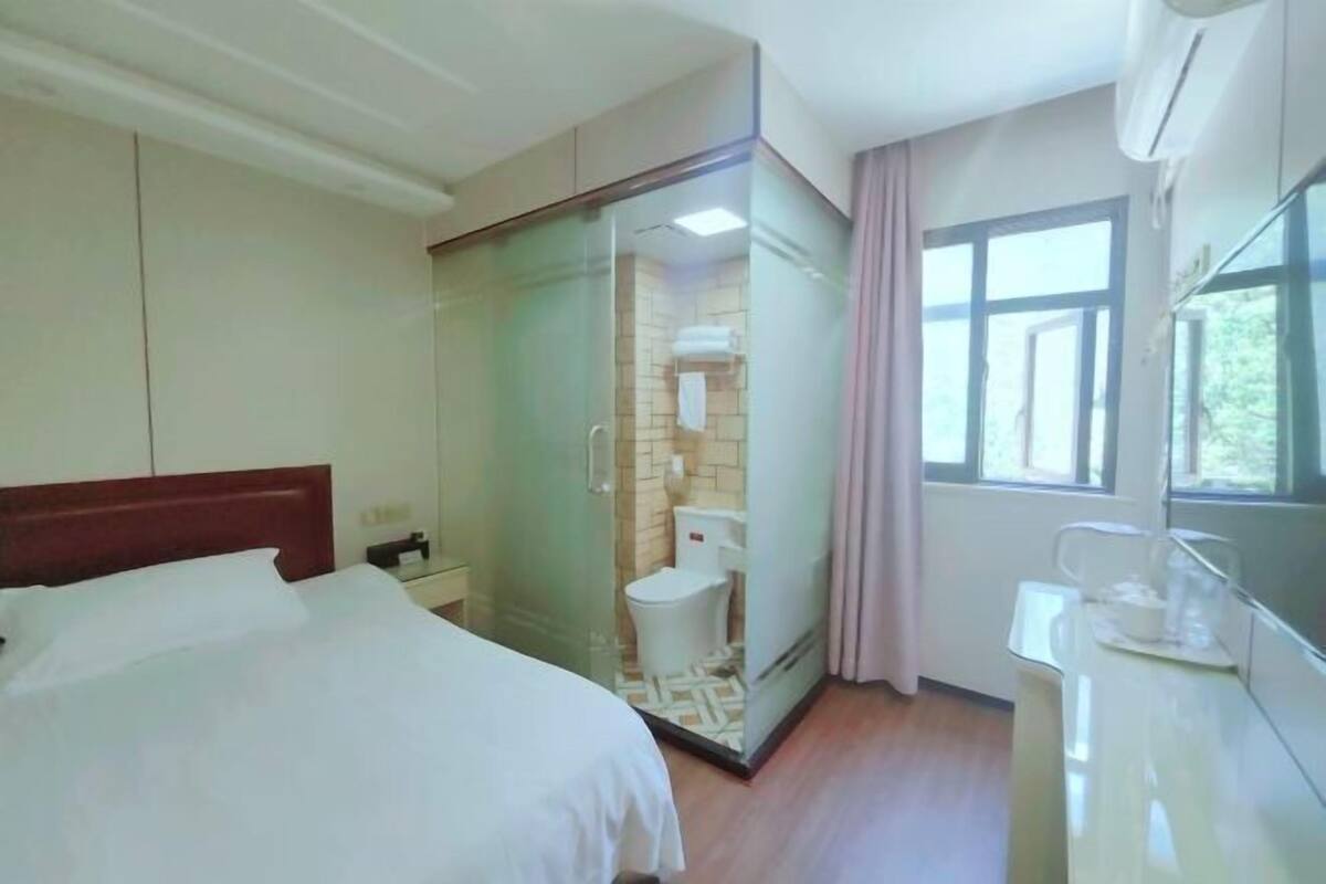 Hotelkamer met een bed, een douchecabine, toilet, wastafel en een raam met gordijnen.