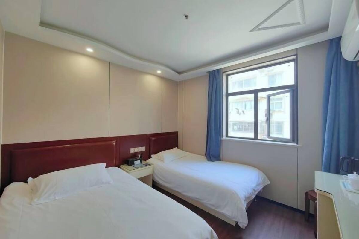 Een hotelkamer met twee bedden, een nachtkastje, een bureau en een raam met gordijnen.