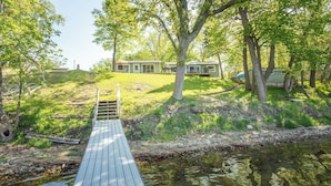 A wooden deck leading to a house with a grassy hill and trees in the background.