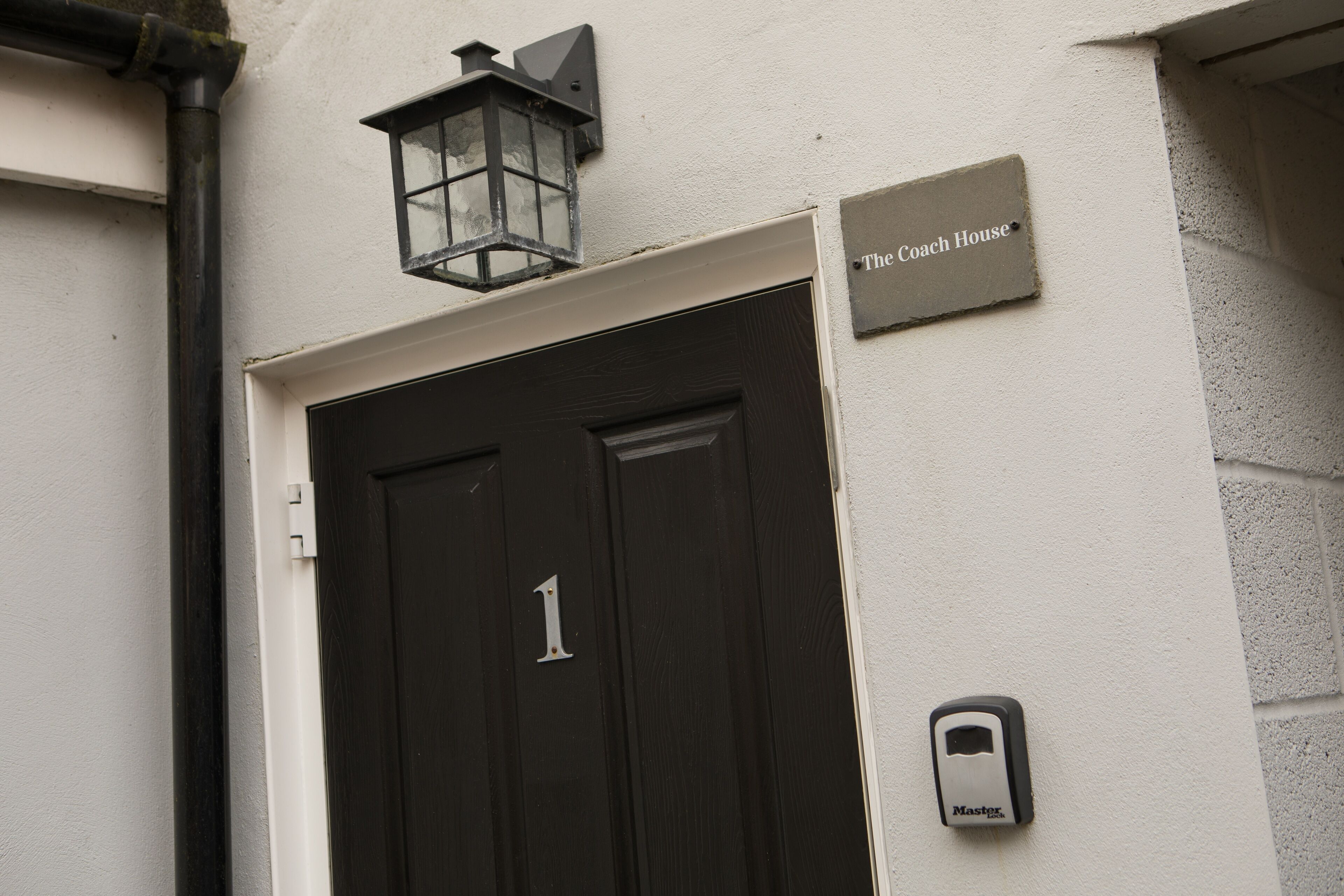 A black door with the number 1, a sign reading "The Coach House", and a doorbell on the wall.