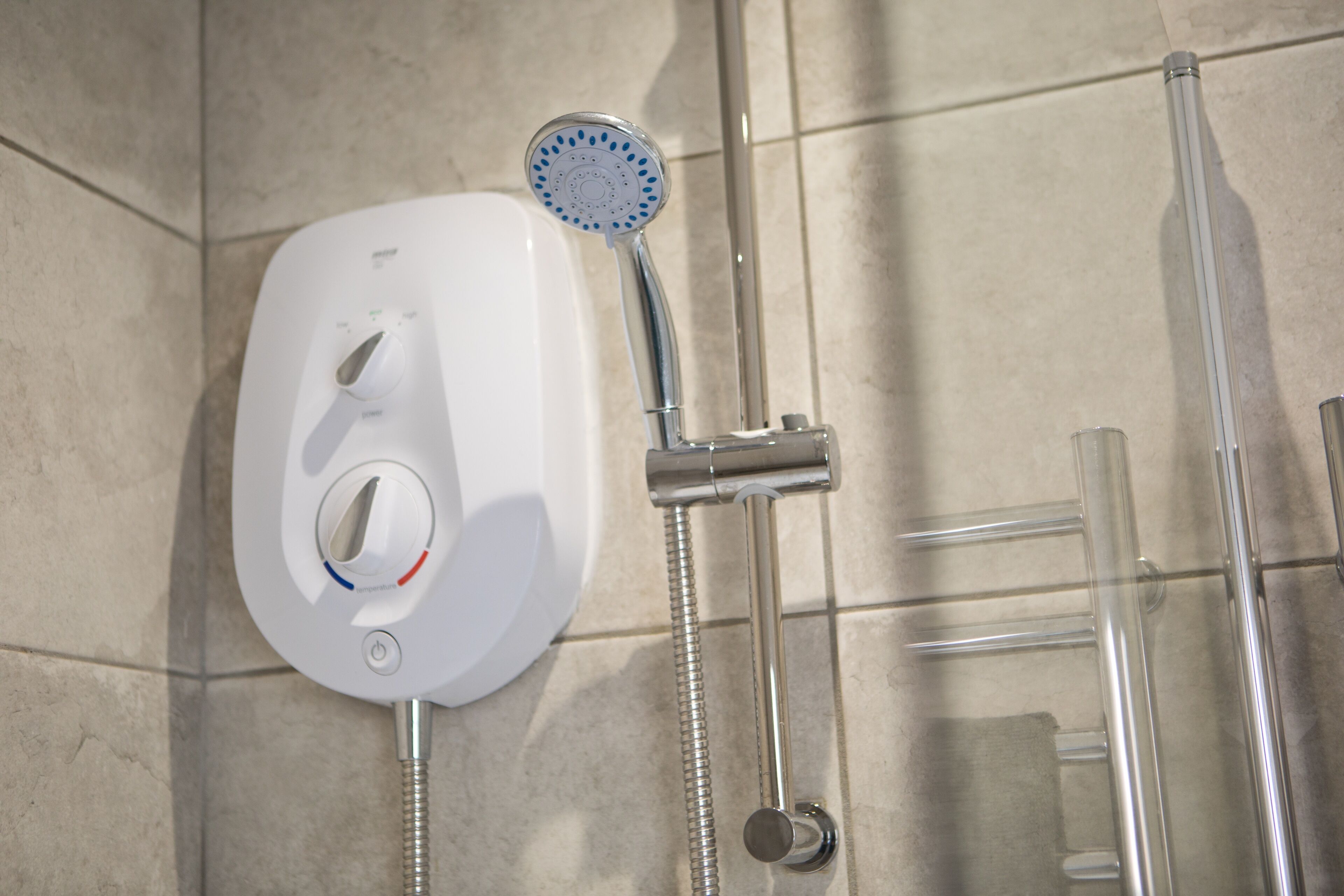 A shower with a handheld showerhead and a wall-mounted control panel.