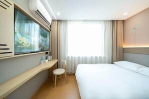 A hotel room with a bed, a desk with a chair, a TV, and a window with curtains.