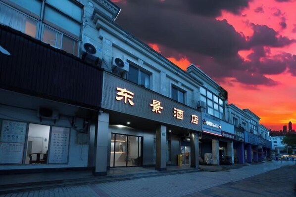 A hotel with a sign in a foreign script, multiple storefronts, and a sunset sky.