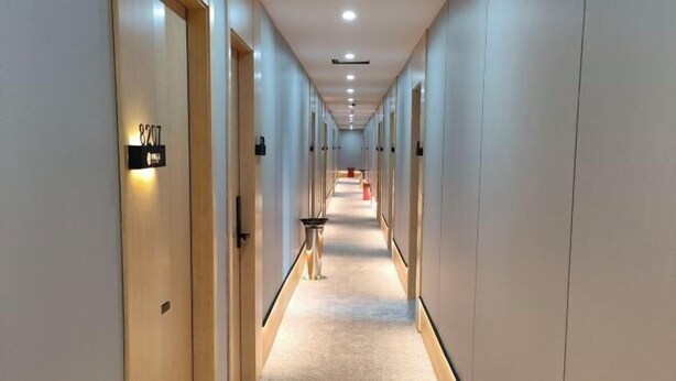 A long, narrow hotel corridor with doors on both sides, a central walkway, and a small table with a chair in the middle. - Dongjing Hotel (Shanghai Shanda College Branch) (Shanghai)