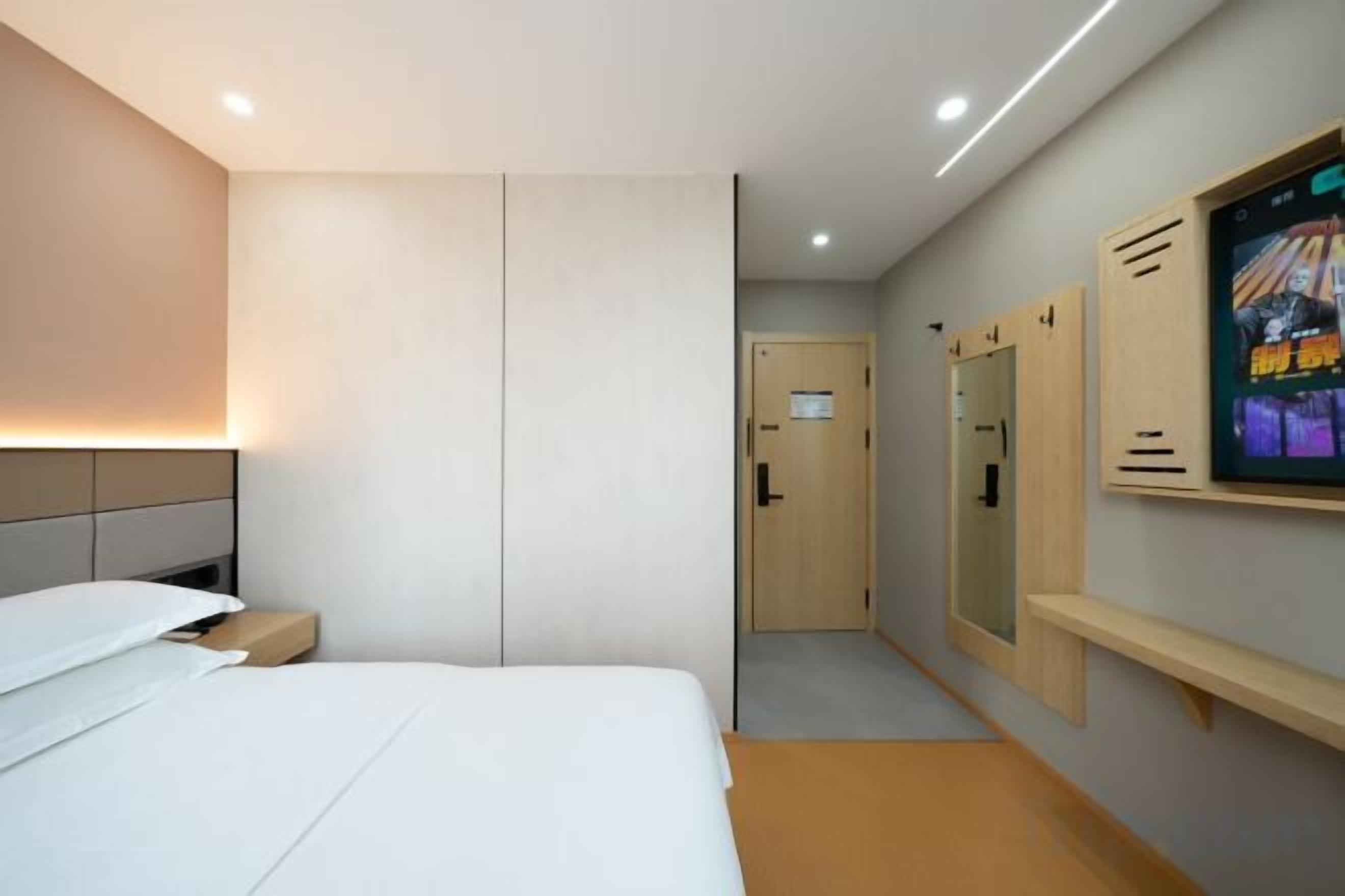 A hotel room with a bed, a bedside table, a TV mounted on the wall, and a door leading to the bathroom.