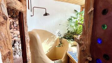 A rustic bathroom with a stone wall, a wooden bathtub, and a wooden ceiling.