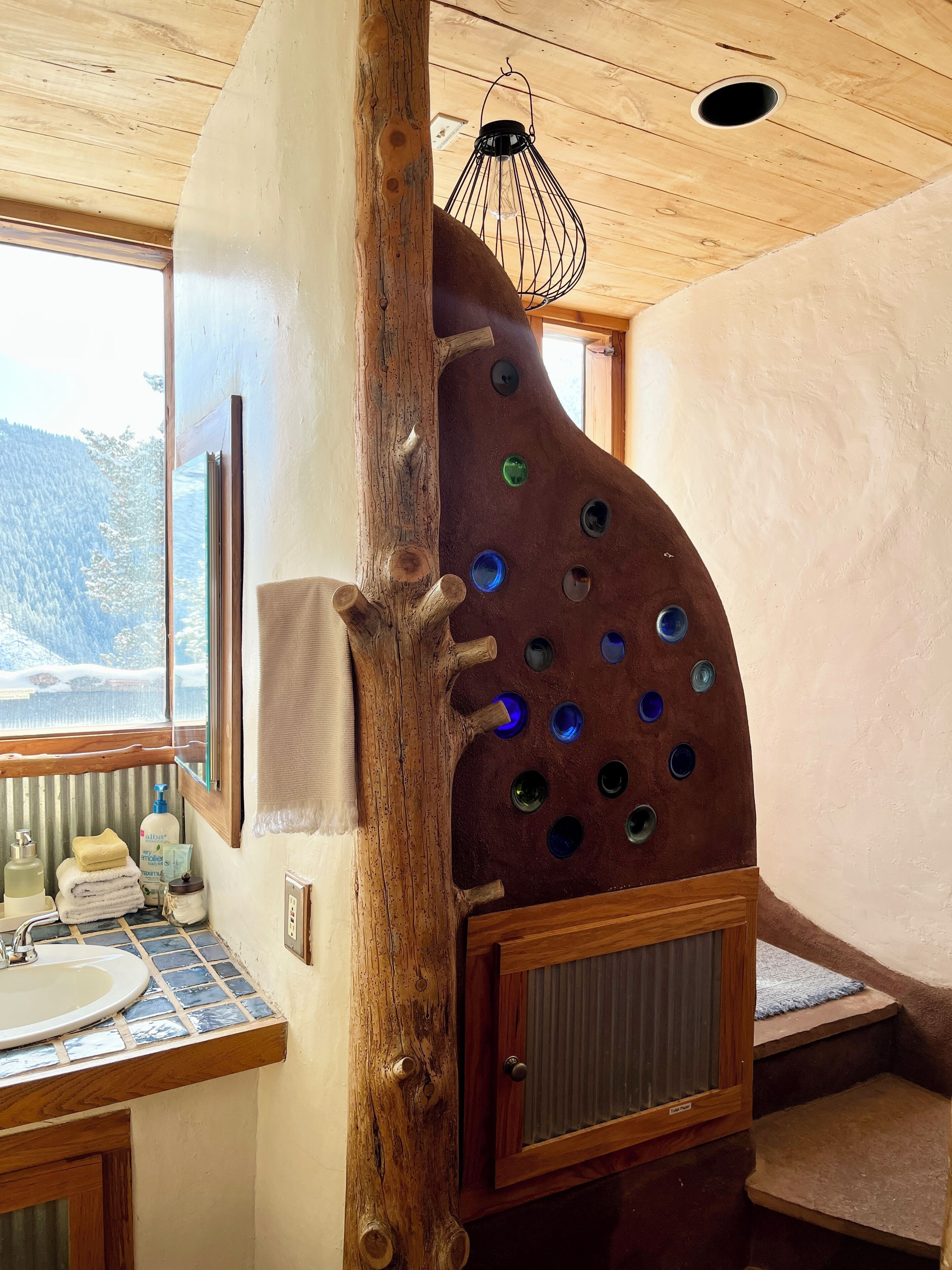 Une salle de bain rustique avec un mur en rondins de bois, un lavabo et une fenêtre donnant sur des montagnes enneigées.
