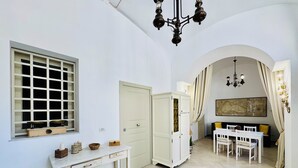 A room with a dining table, chairs, a white cabinet, a window with a grid pattern, and a chandelier. - YourHome - Antico Casale Sorrentino (Meta)