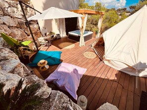 A wooden deck with a hot tub, outdoor furniture, and a tent.