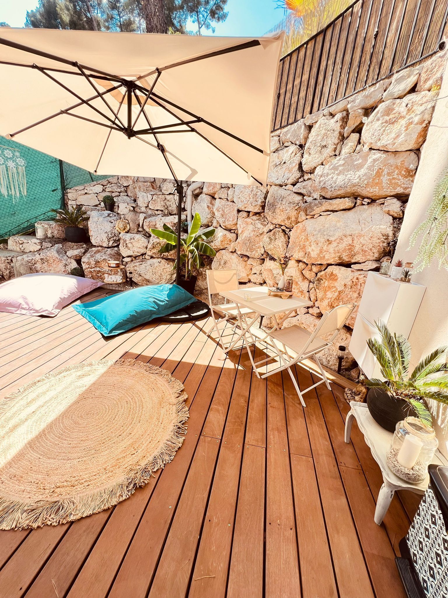 Een houten terras met een hangmat, een tafel en stoelen onder een overkapping.
