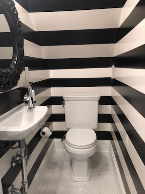 Ein Badezimmer mit Wandgestaltung in Schwarz und Weißstreifen, einem weißen Waschbecken und einer Toilette.