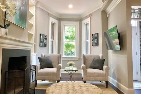 A living room with two armchairs, a fireplace, and a large window with a view of greenery.