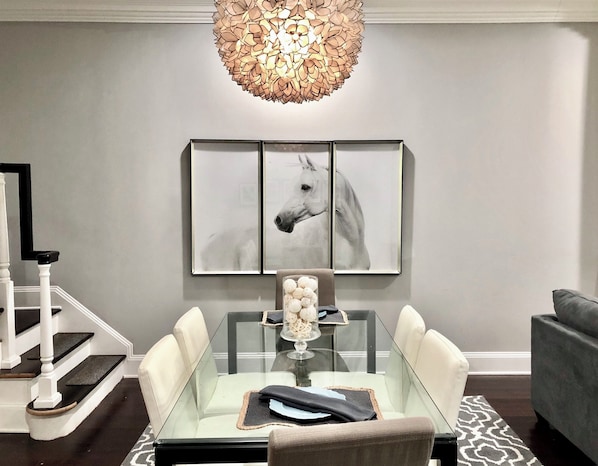 A dining area with a glass table, white chairs, a chandelier, and a framed horse artwork on the wall. - 5 Blocks to US Capitol, Renovated 1895 Capitol Hill Victorian (Washington)