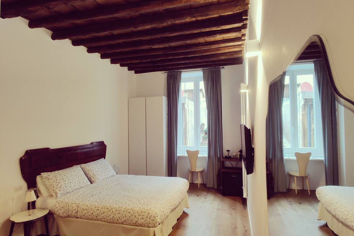 A bedroom with a wooden ceiling, two beds, a chair, and a desk.