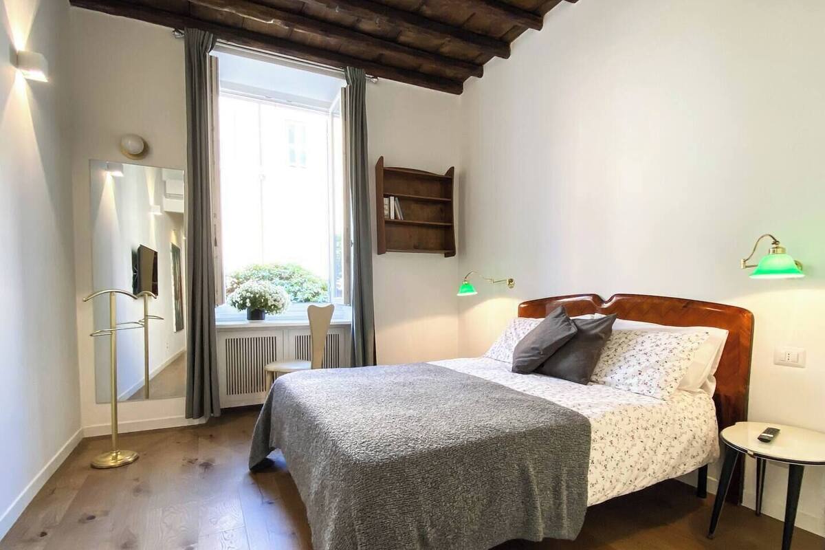 A bedroom with a wooden bed, a bedside table, a mirror, a window with curtains, and a radiator.