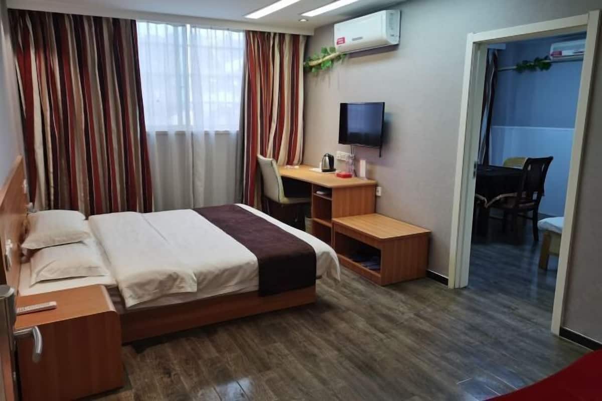 A hotel room with a bed, desk, chair, TV, and an air conditioning unit.